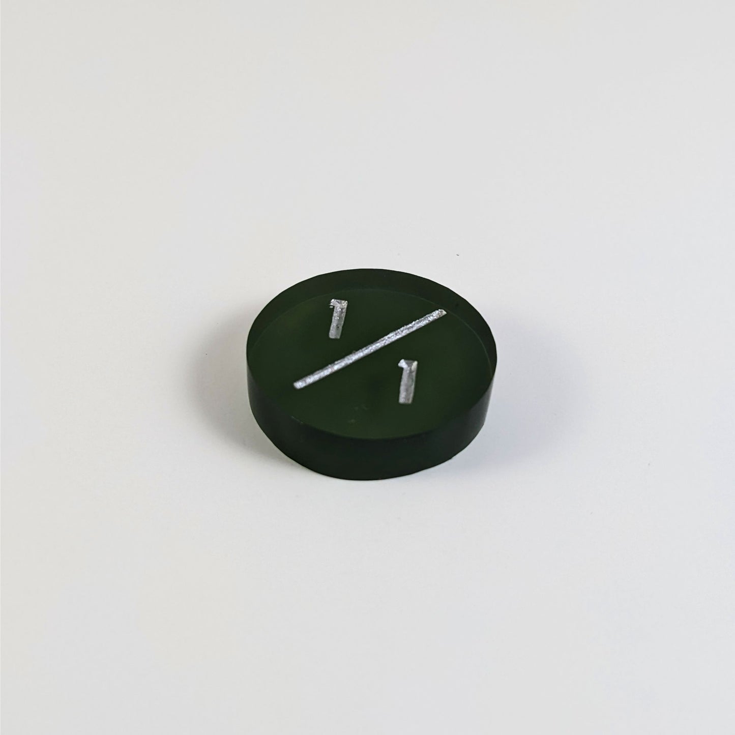 A low angle photo of a dark green 1/1 token with silver numbers sits on a white background.