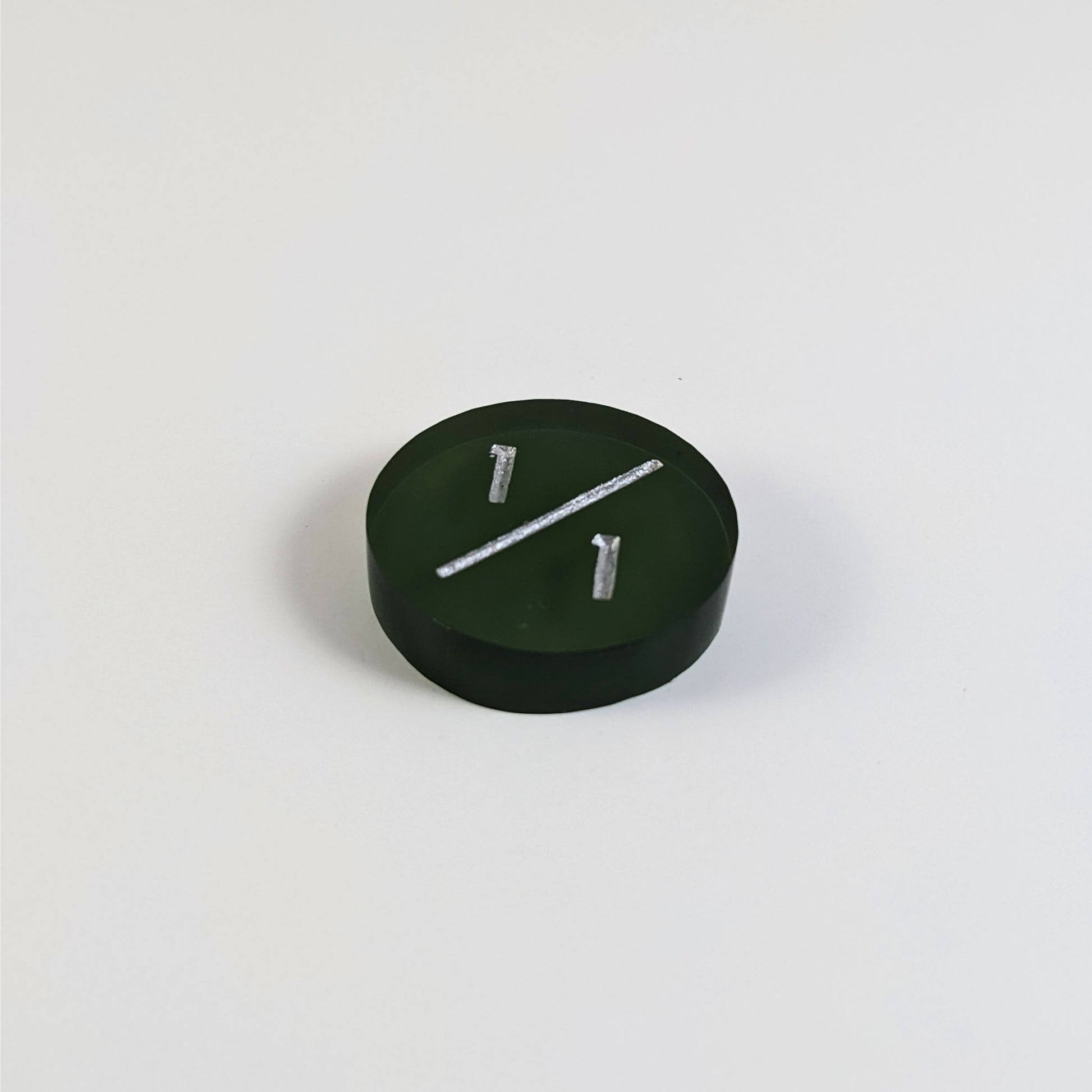A low angle photo of a dark green 1/1 token with silver numbers sits on a white background.