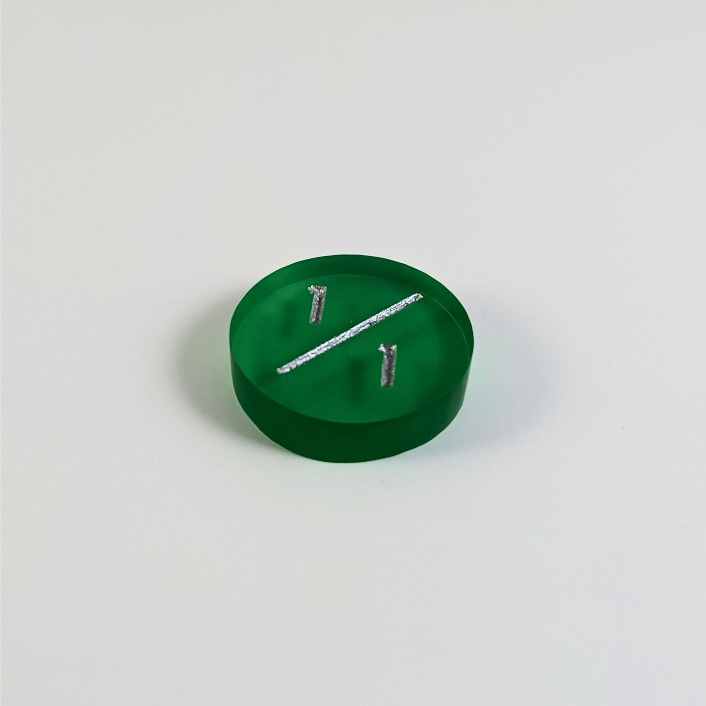 A low angle photo of a green 1/1 token with silver numbers sits on a white background.