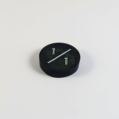 A low angle photo of a black and green 1/1 token with silver numbers sits on a white background.