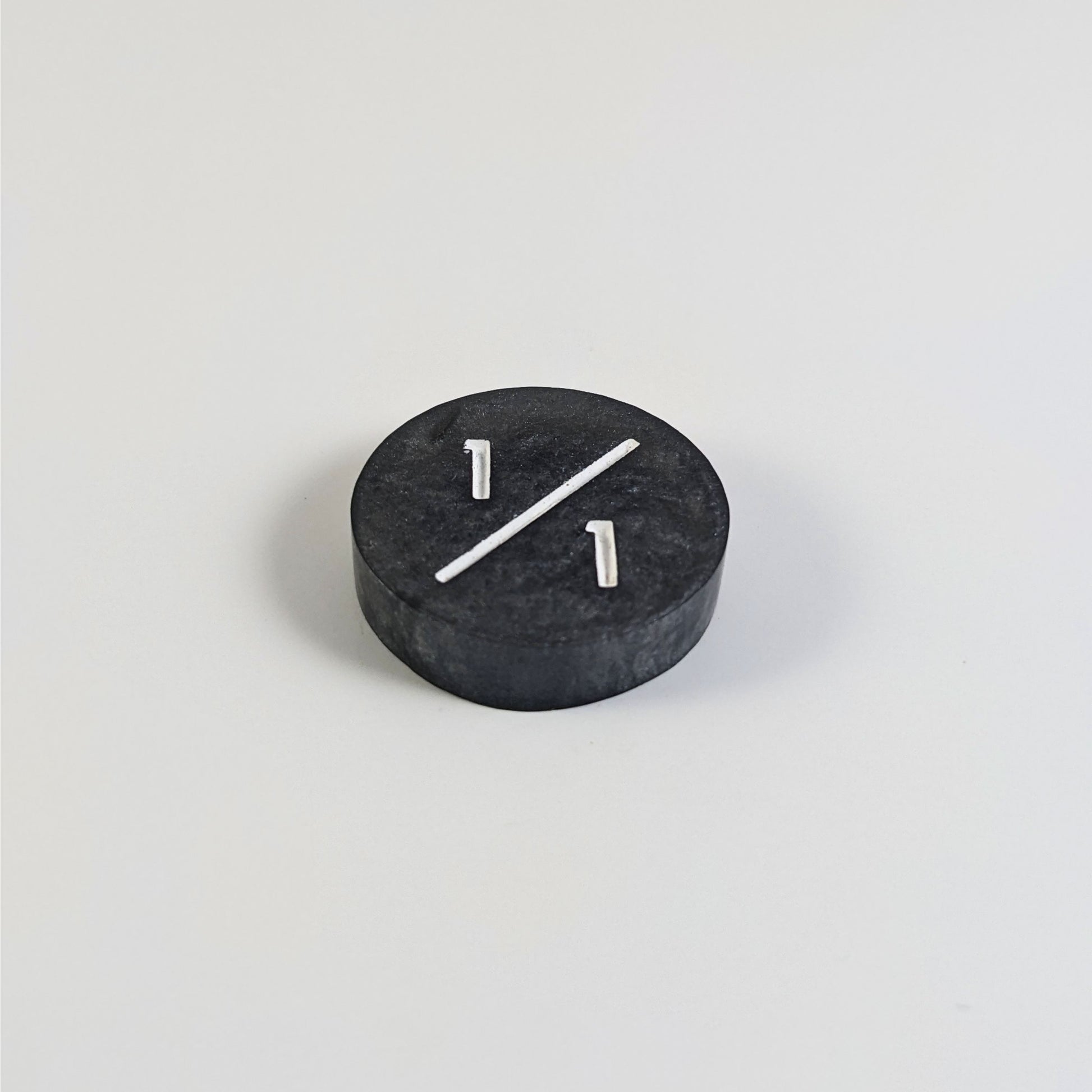 A low angle photo of a silver 1/1 token with white numbers sits on a white background.