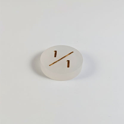 A low angle photo of a white 1/1 token with gold numbers sits on a white background.