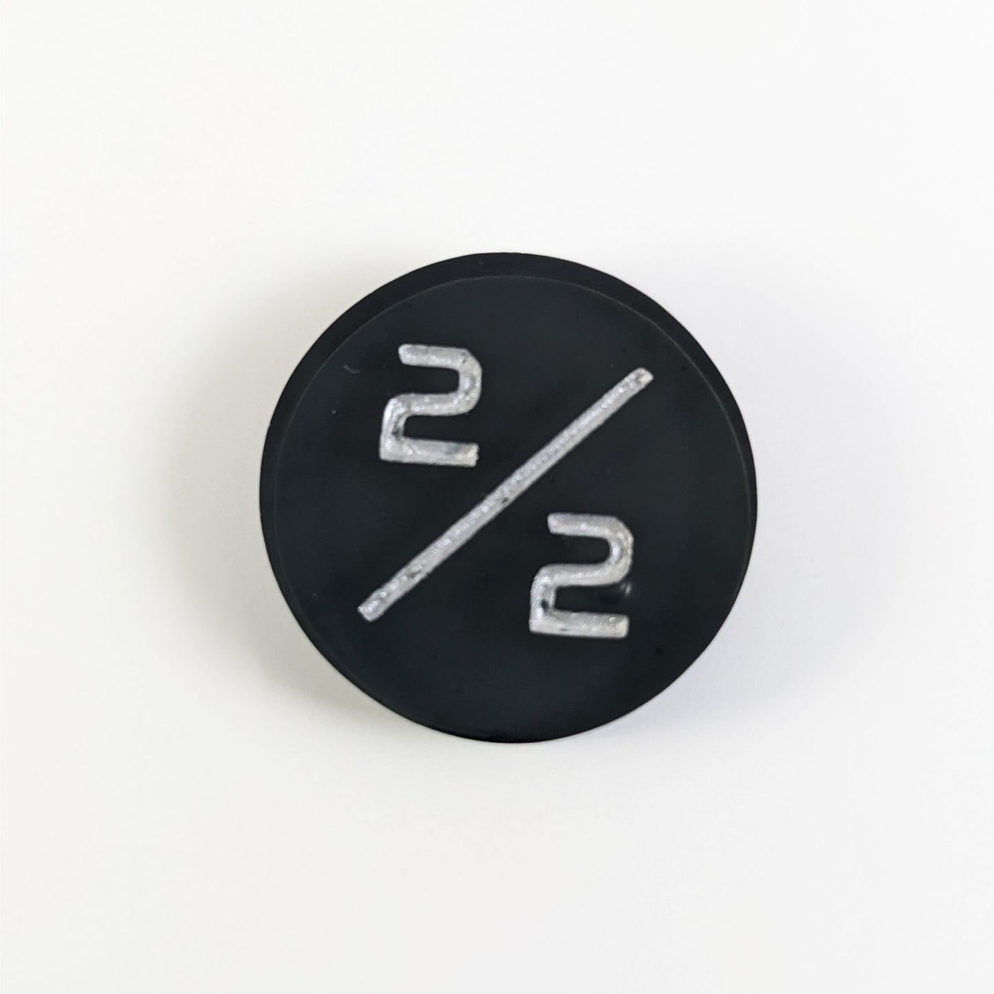 A top down photo of a black 2/2 token with silver numbers sits on a white background. A bubble is visible near the bottom 2 but it is on the back side of the token.