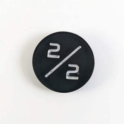 A top down photo of a black 2/2 token with silver numbers sits on a white background. A bubble is visible near the bottom 2 but it is on the back side of the token.