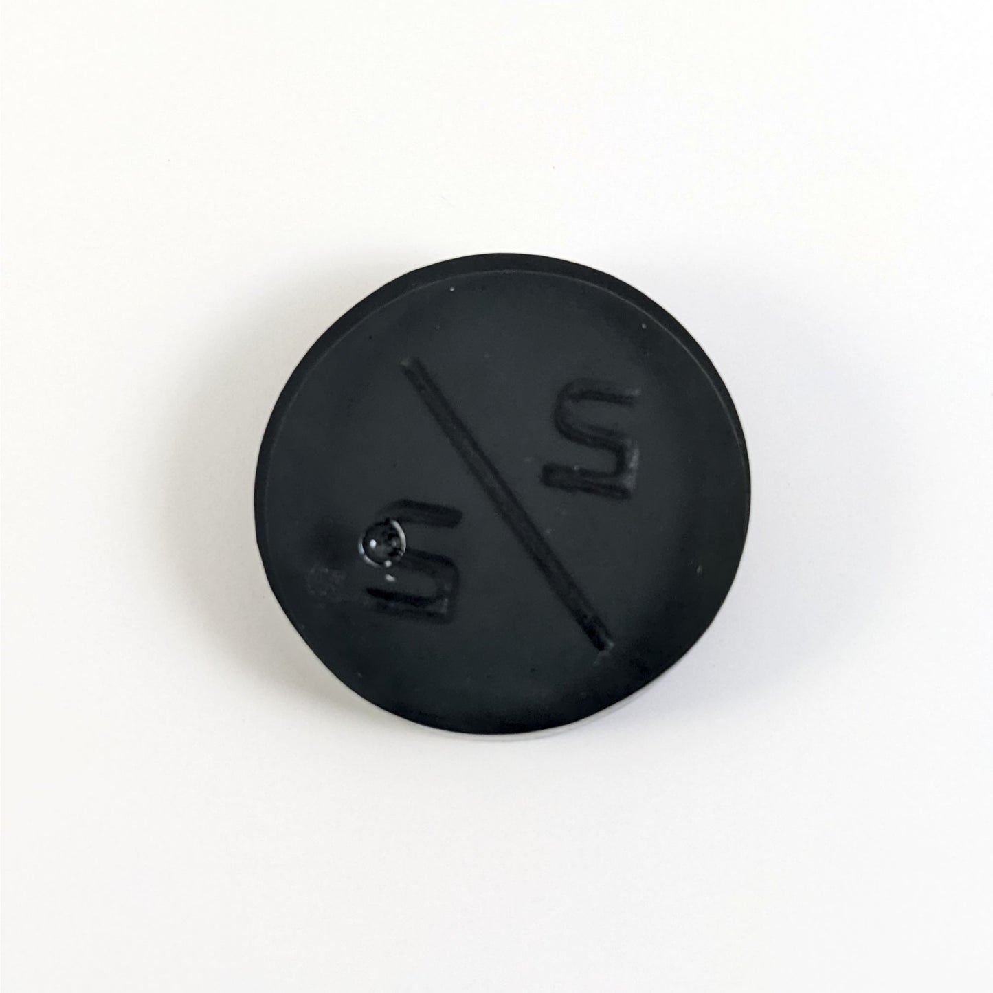 A top down photo of the back of a black 2/2 token with silver numbers sitting on a white background. A bubble is visible.