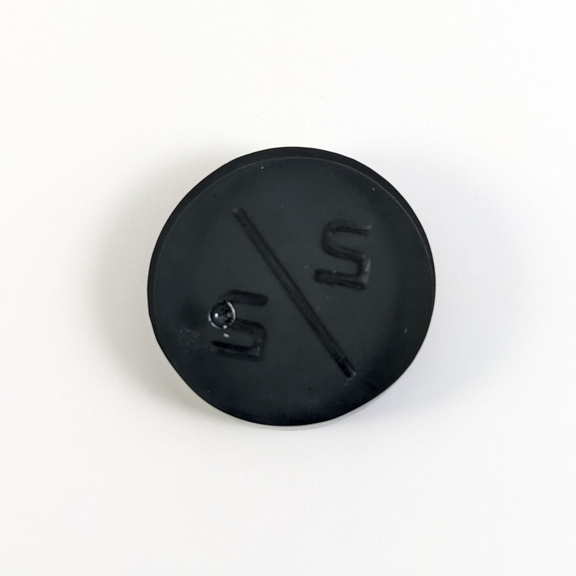 A top down photo of the back of a black 2/2 token with silver numbers sitting on a white background. A bubble is visible.