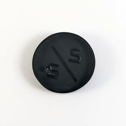 A top down photo of the back of a black 2/2 token with silver numbers sitting on a white background. A bubble is visible.