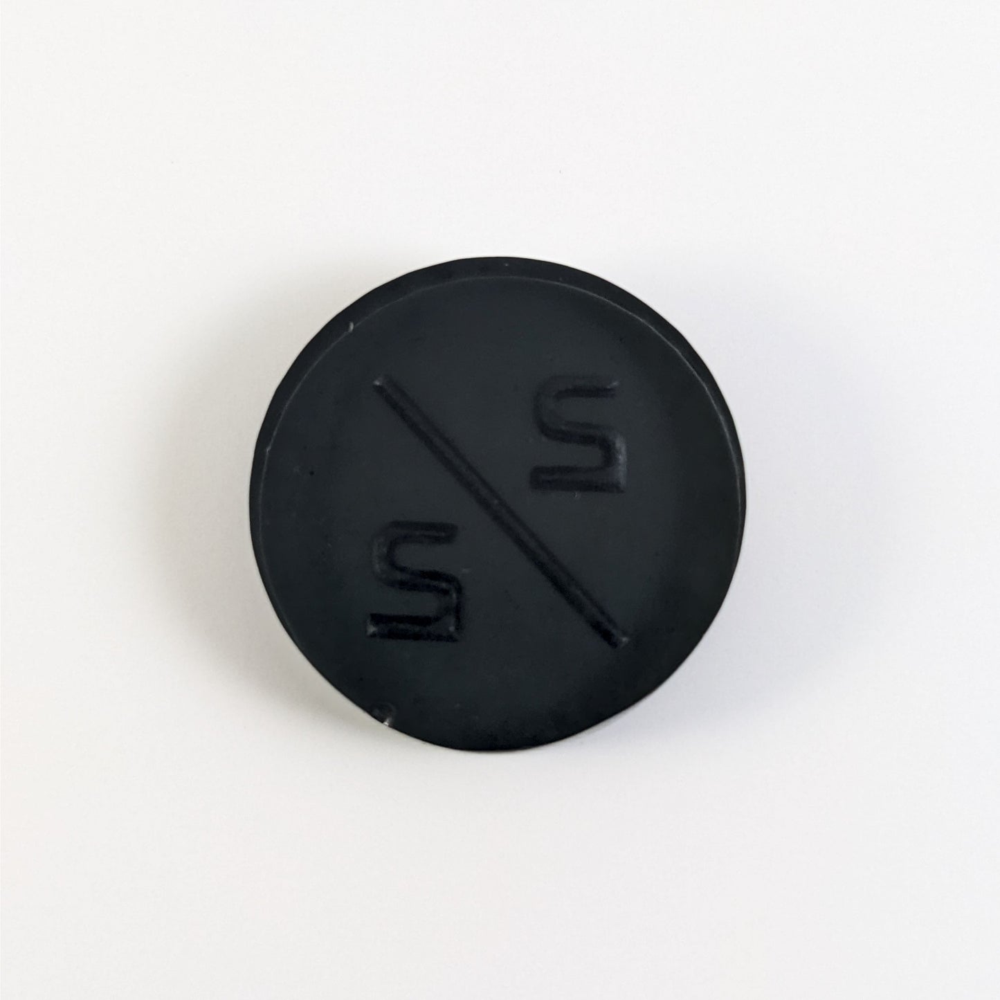 A top down photo of the back of a black 2/2 token with silver numbers sitting on a white background. A bubble is visible on the bottom edge.