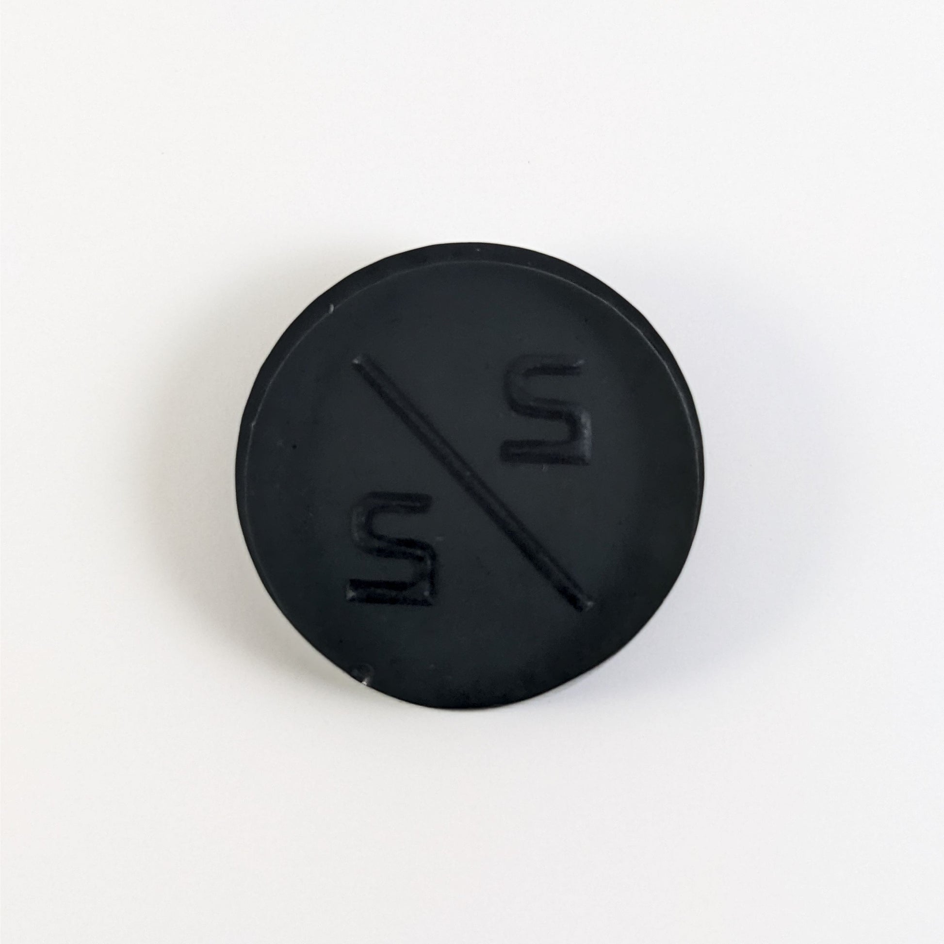 A top down photo of the back of a black 2/2 token with silver numbers sitting on a white background. A bubble is visible on the bottom edge.
