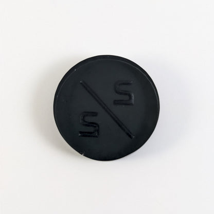 A top down photo of the back of a black 2/2 token with silver numbers sitting on a white background. A bubble is visible on the bottom edge.