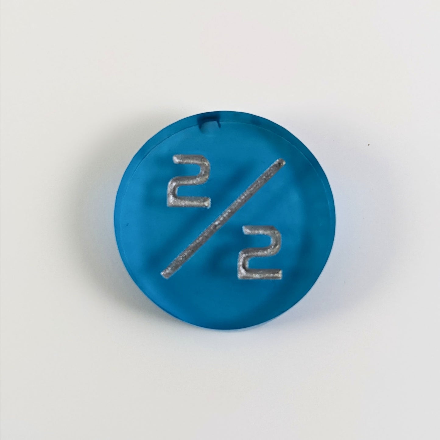 A top down photo of a black 2/2 token with silver numbers sits on a white background. A bubble is visible near the top on the edge but it is on the back side of the token.