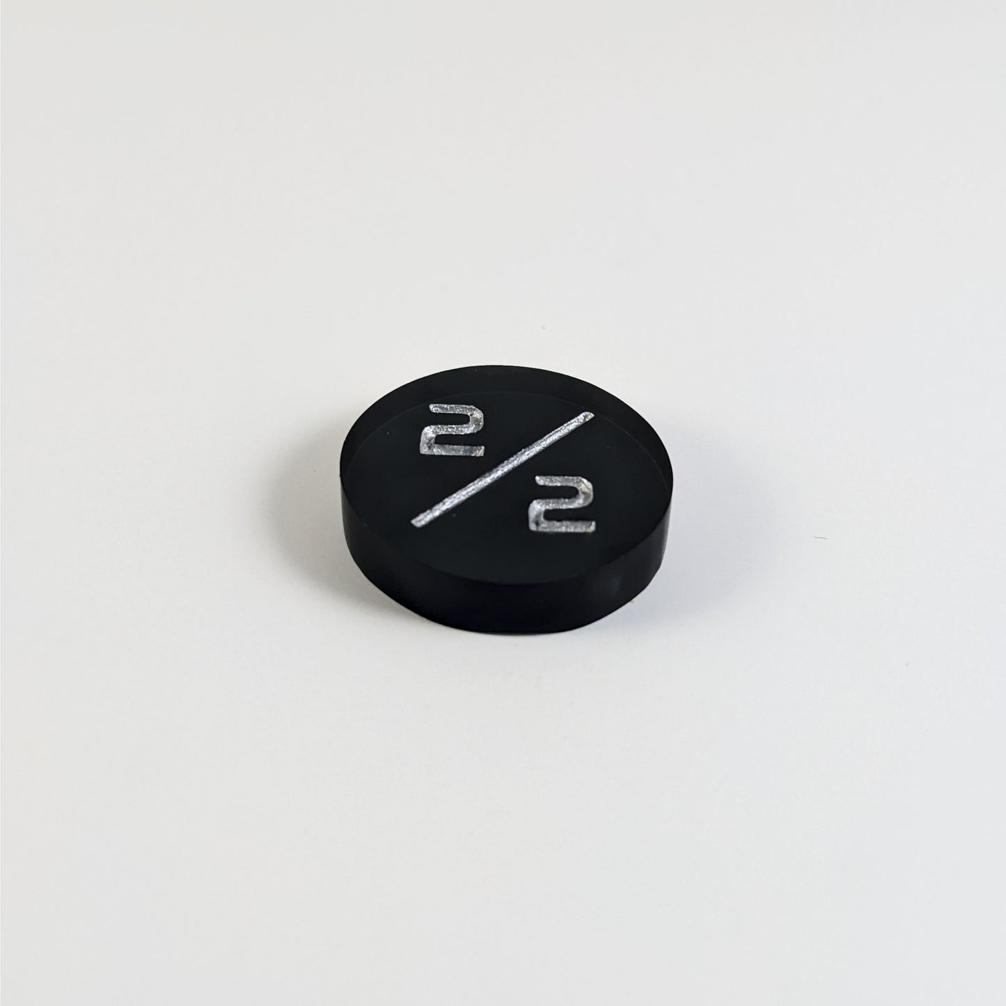 A low angle photo of a black 2/2 token with silver numbers sits on a white background. The cosmetic flaw is not apparently visible at this angle.