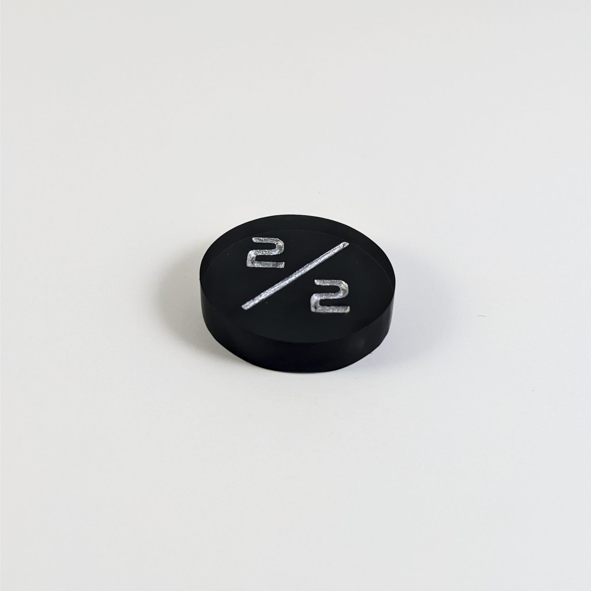 A low angle photo of a black 2/2 token with silver numbers sits on a white background. The cosmetic flaw is not apparently visible at this angle.