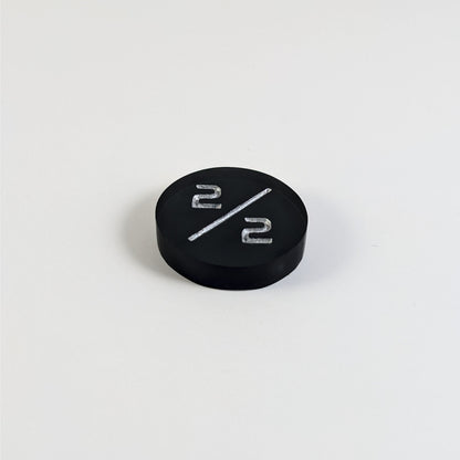 A low angle photo of a black 2/2 token with silver numbers sits on a white background. The cosmetic flaw is not apparently visible at this angle.