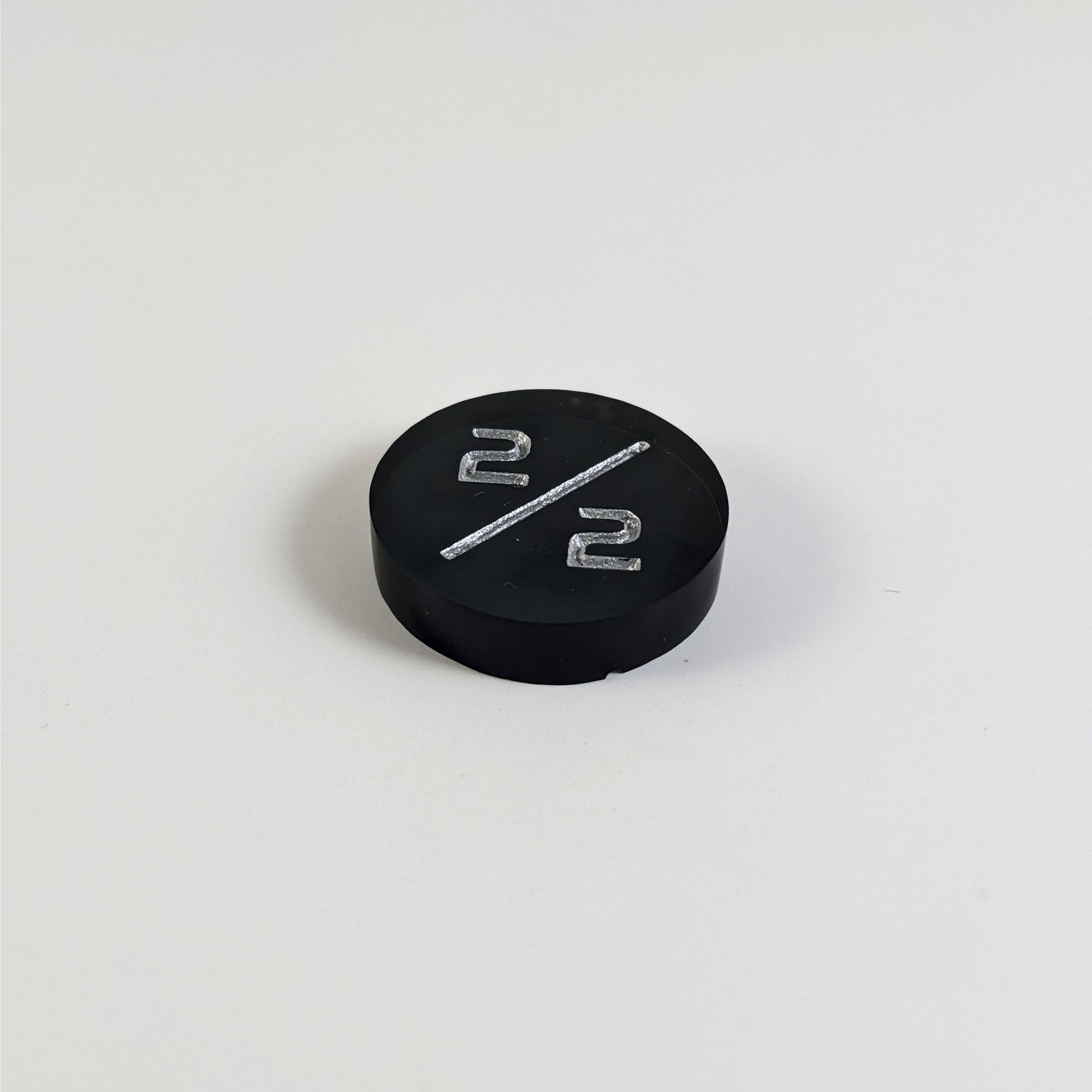 A low angle photo of a black 2/2 token with silver numbers sits on a white background. The small bubble is on the bottom edge of the token under the bottom 2.