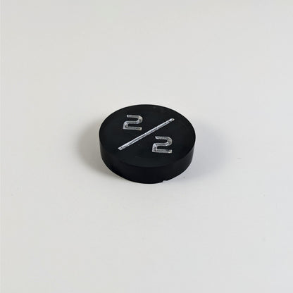 A low angle photo of a black 2/2 token with silver numbers sits on a white background. The small bubble is on the bottom edge of the token under the bottom 2.