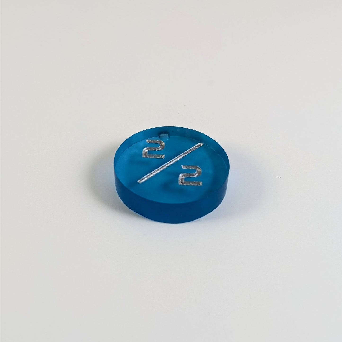 A low angle photo of a blue 2/2 token with silver numbers sits on a white background. The bubble is visible above the top 2 and is on the back of the token.