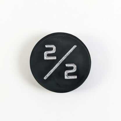 A top down photo of a black 2/2 token with silver numbers sits on a white background.
