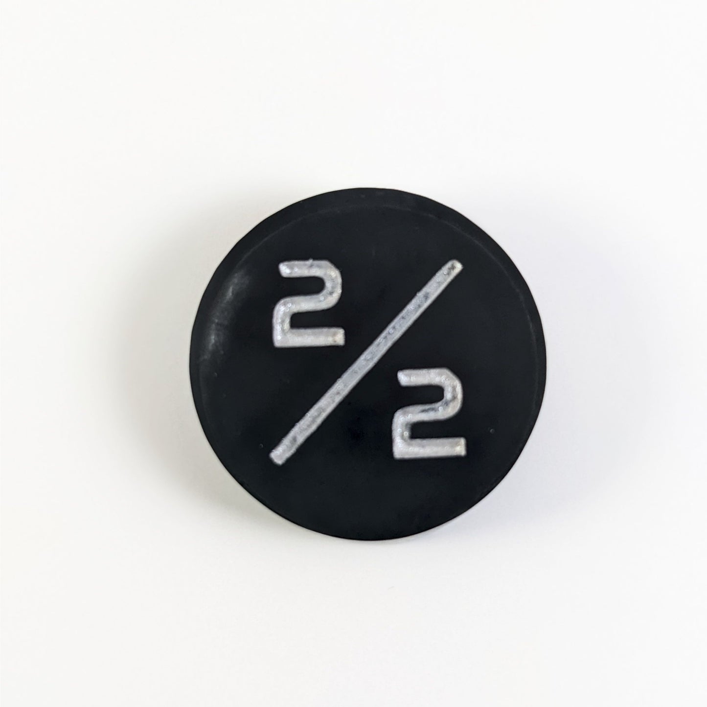 A top down photo of a black with a silver spot 2/2 token with silver numbers sits on a white background.