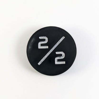 A top down photo of a black with a silver spot 2/2 token with silver numbers sits on a white background.