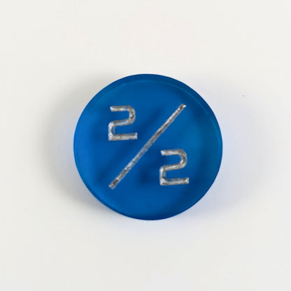 A top down photo of a blue 2/2 token with silver numbers sits on a white background.