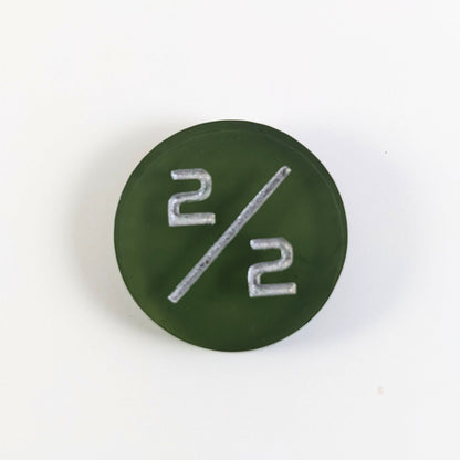 A top down photo of a dark green 2/2 token with silver numbers sits on a white background.