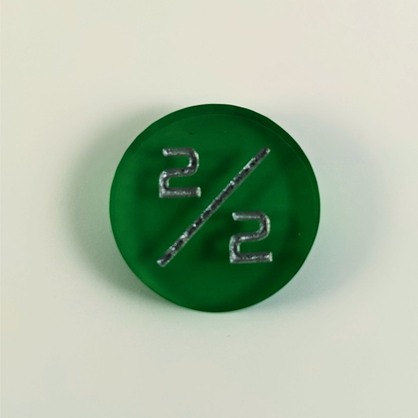 A top down photo of a green 2/2 token with silver numbers sits on a white background.