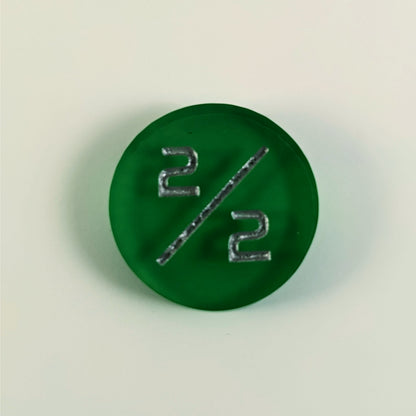 A top down photo of a green 2/2 token with silver numbers sits on a white background.