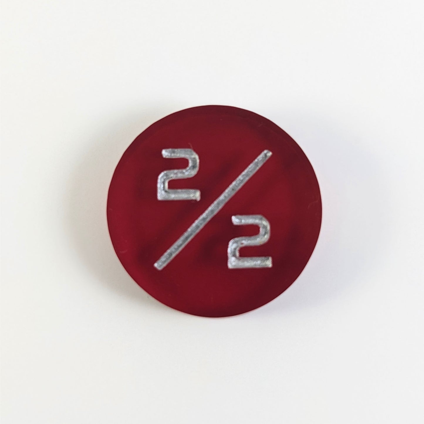A top down photo of a red 2/2 token with silver numbers sits on a white background.
