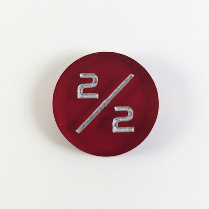 A top down photo of a red 2/2 token with silver numbers sits on a white background.