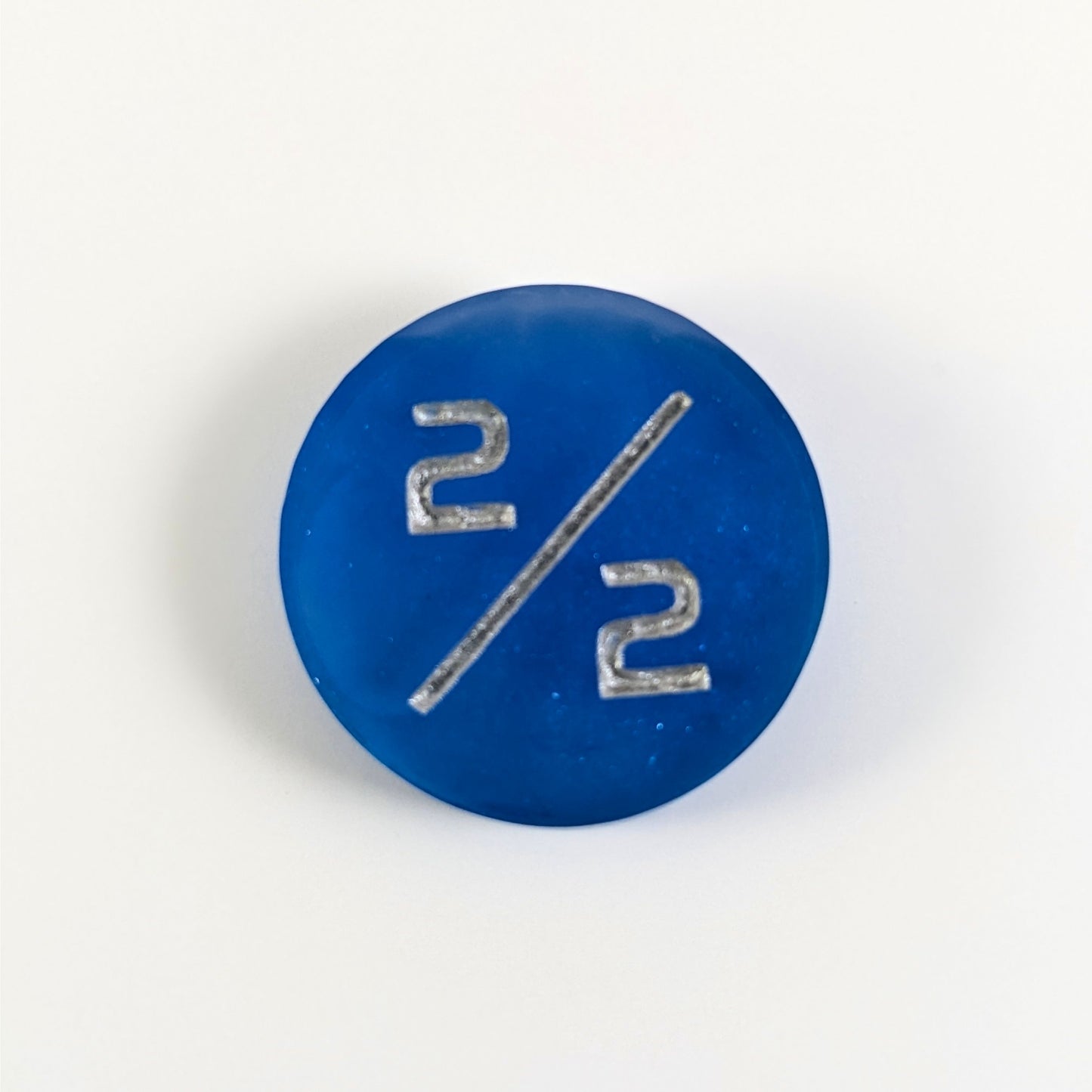 A top down photo of a sapphire blue 2/2 token with silver numbers sits on a white background.