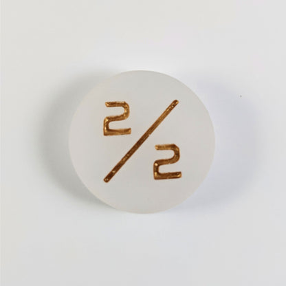 A top down photo of a white 2/2 token with gold numbers sits on a white background.