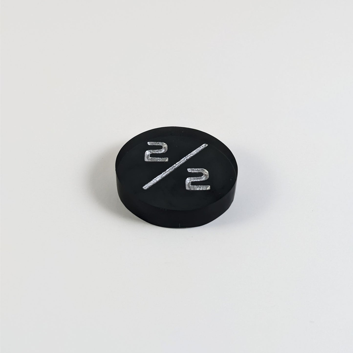 A low angle photo of a black 2/2 token with silver numbers sits on a white background.