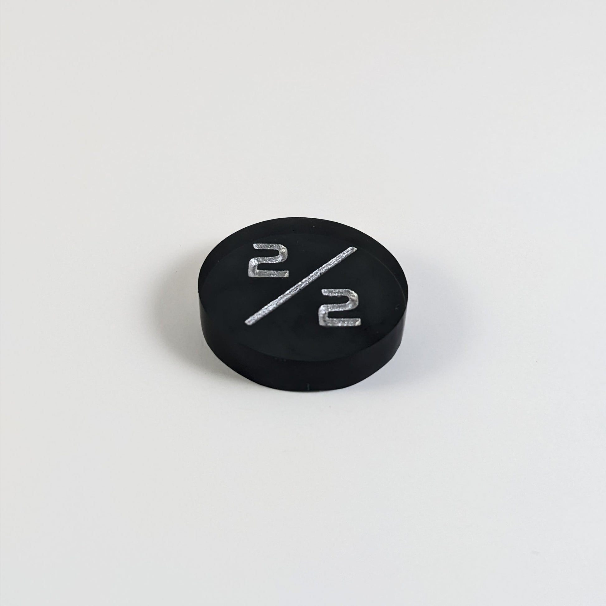 A low angle photo of a black 2/2 token with silver numbers sits on a white background.