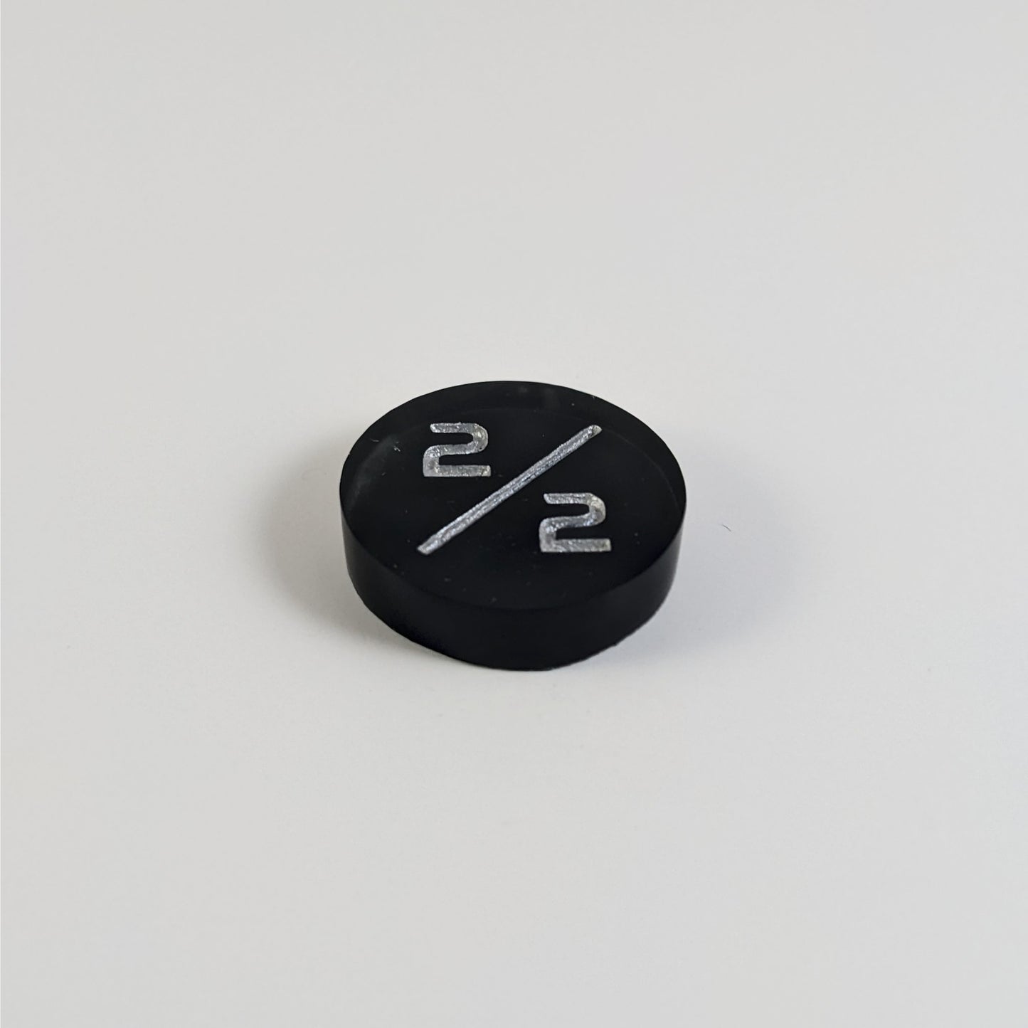 A low angle photo of a black with a silver spot 2/2 token with silver numbers sits on a white background.