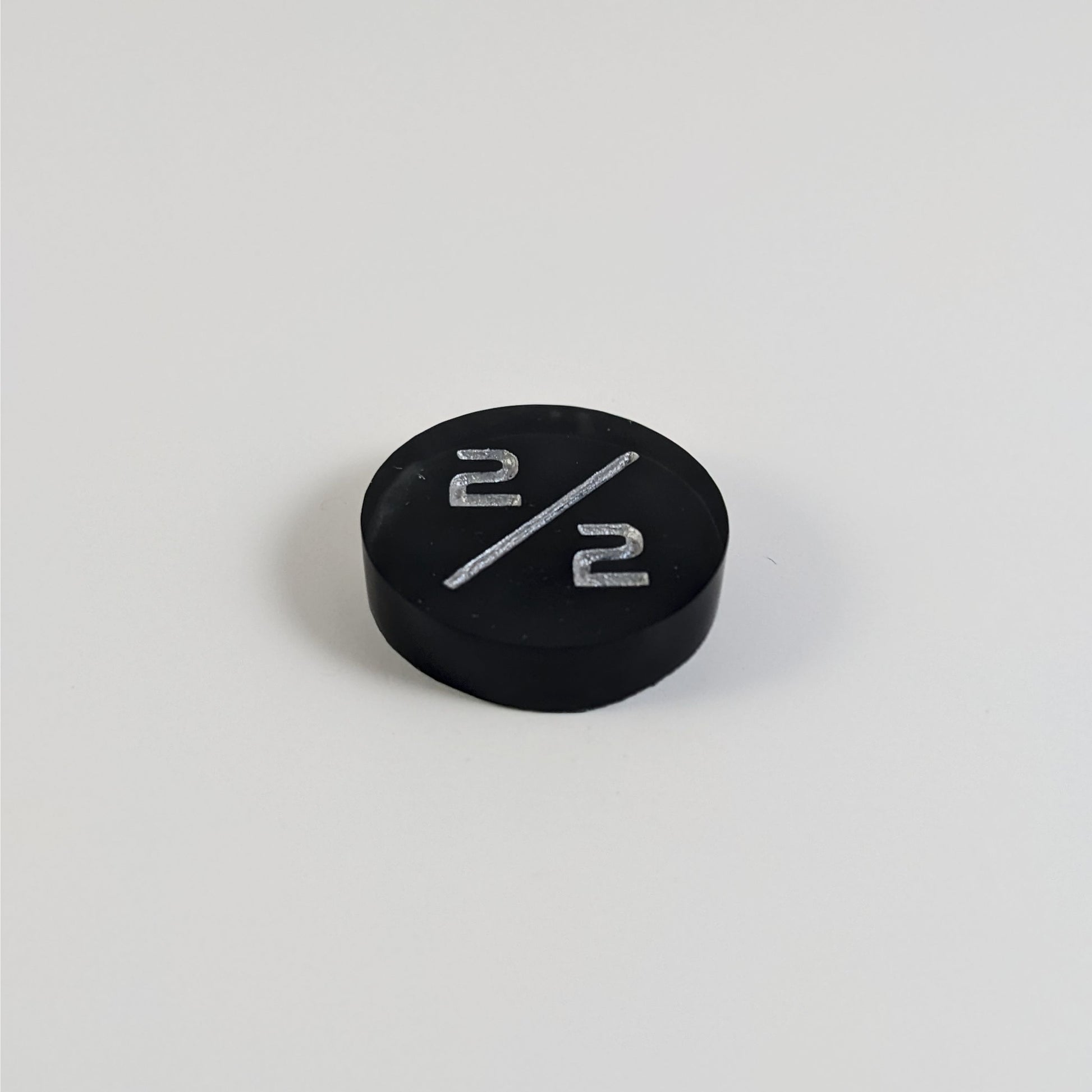 A low angle photo of a black with a silver spot 2/2 token with silver numbers sits on a white background.
