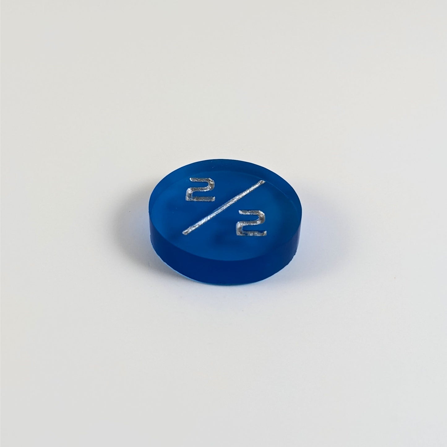 A low angle photo of a blue 2/2 token with silver numbers sits on a white background.