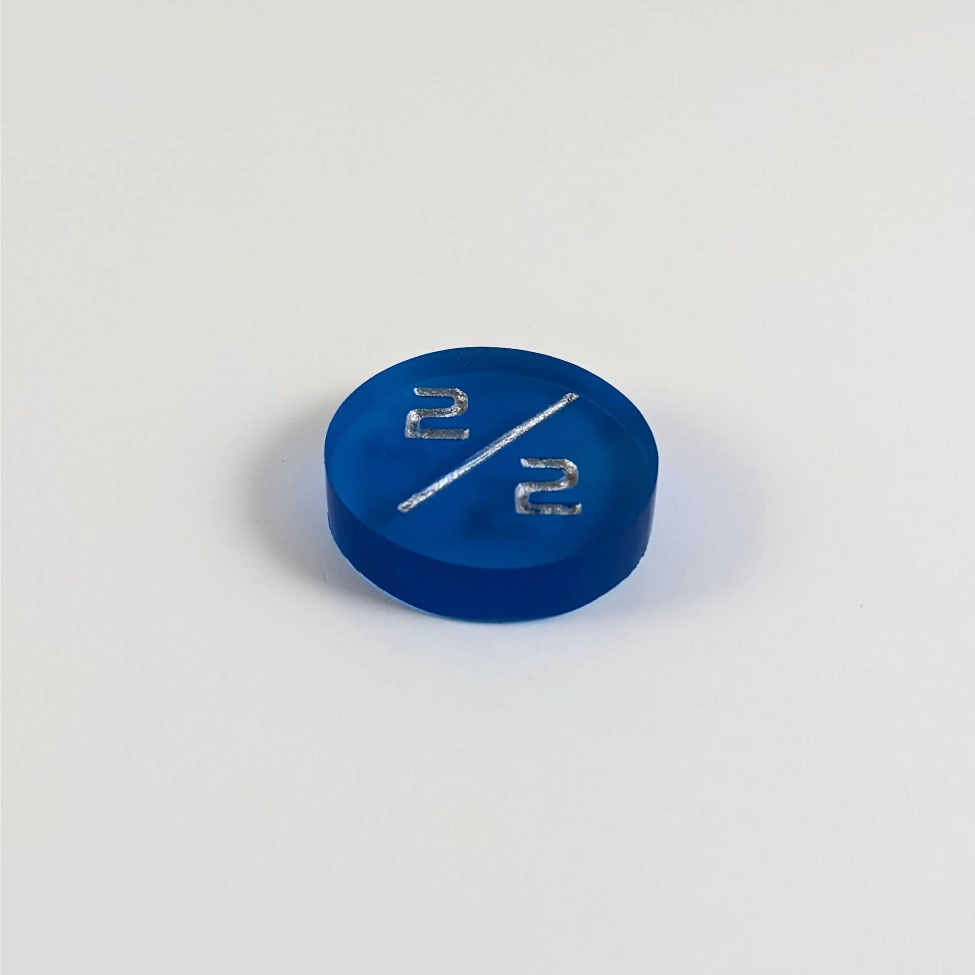 A low angle photo of a blue 2/2 token with silver numbers sits on a white background.