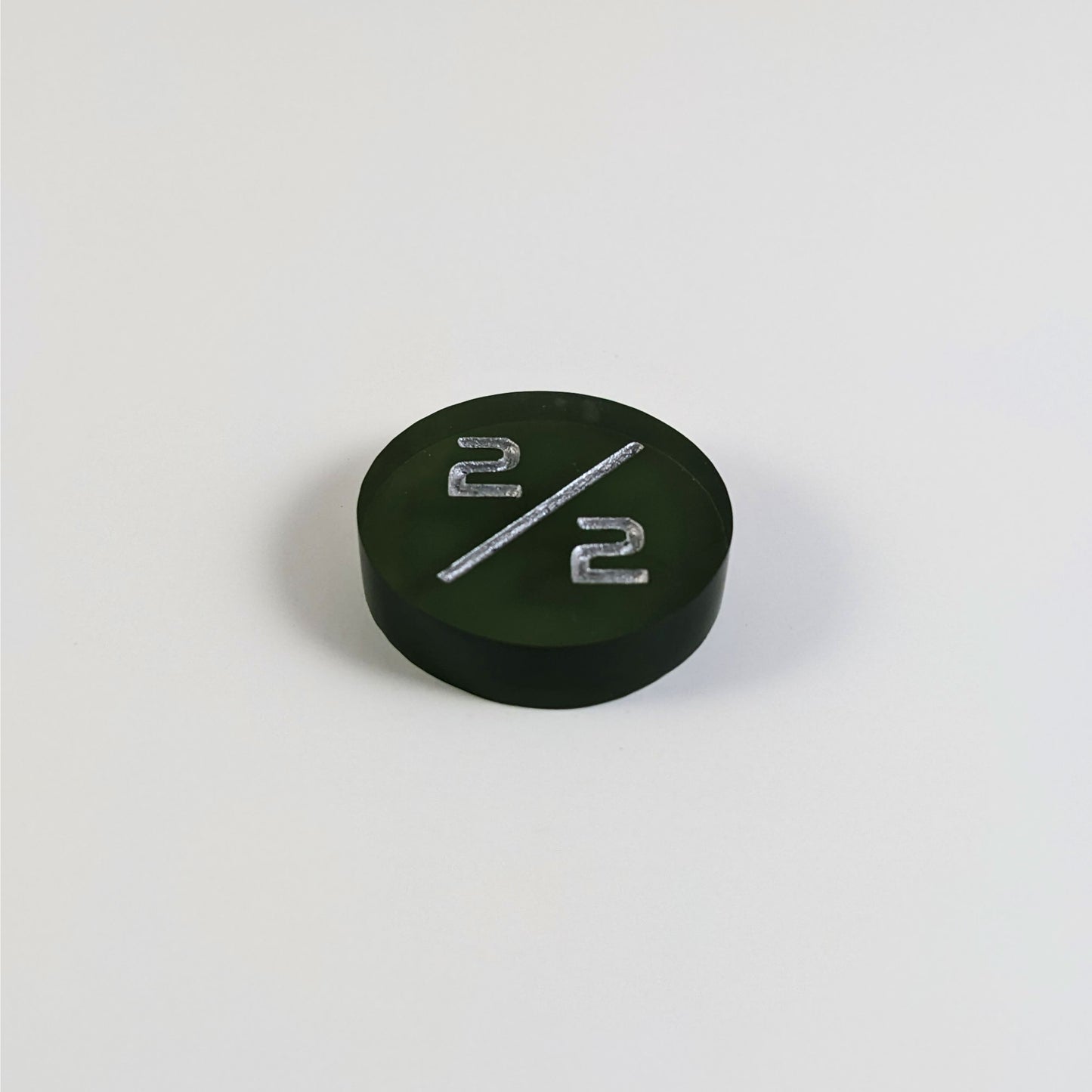 A low angle photo of a dark green 2/2 token with silver numbers sits on a white background.