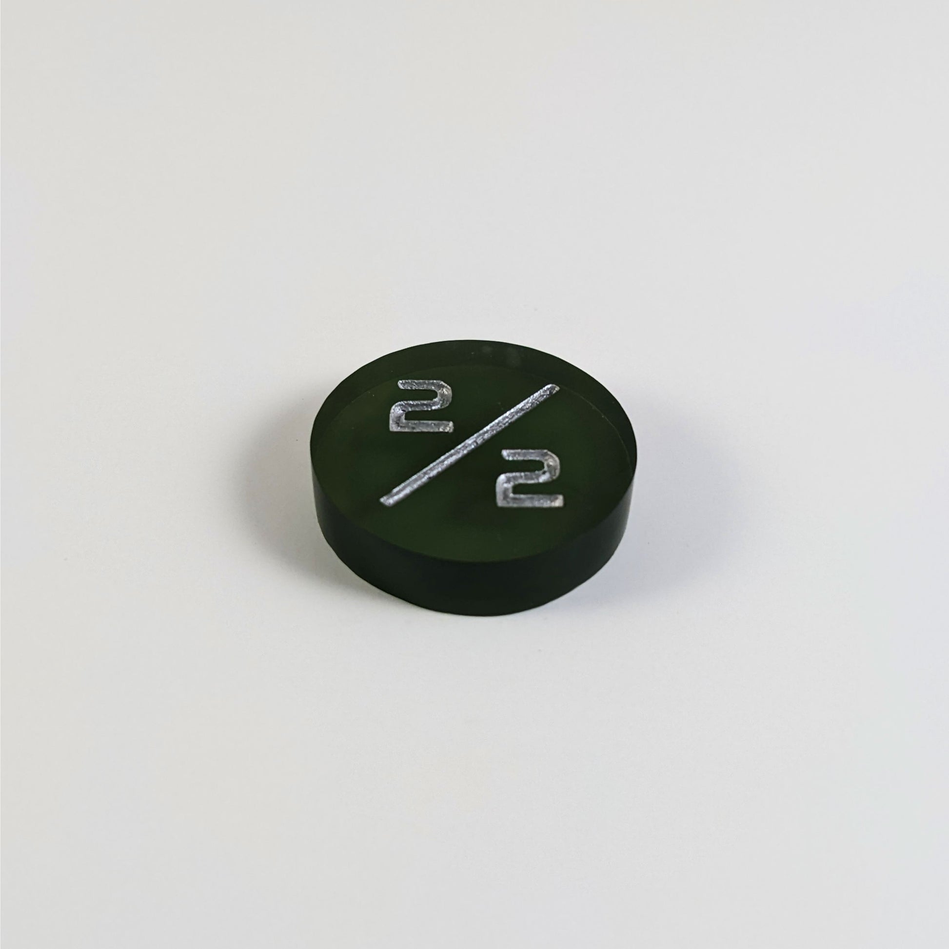 A low angle photo of a dark green 2/2 token with silver numbers sits on a white background.