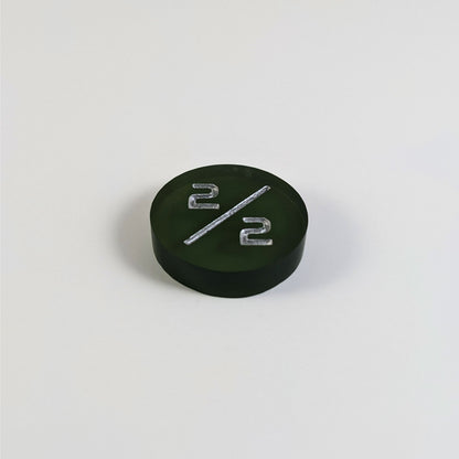 A low angle photo of a dark green 2/2 token with silver numbers sits on a white background.