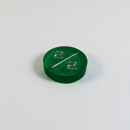 A low angle photo of a green 2/2 token with silver numbers sits on a white background.