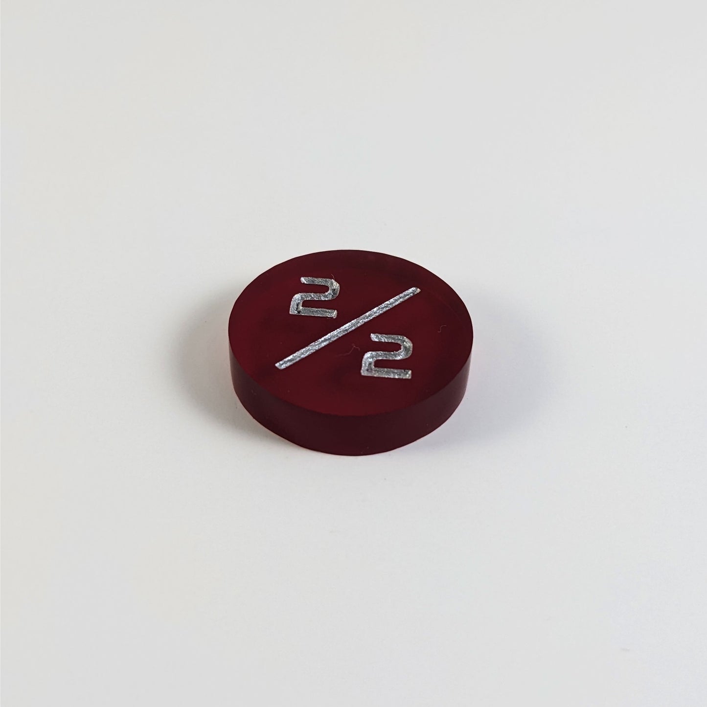 A low angle photo of a red 2/2 token with silver numbers sits on a white background.