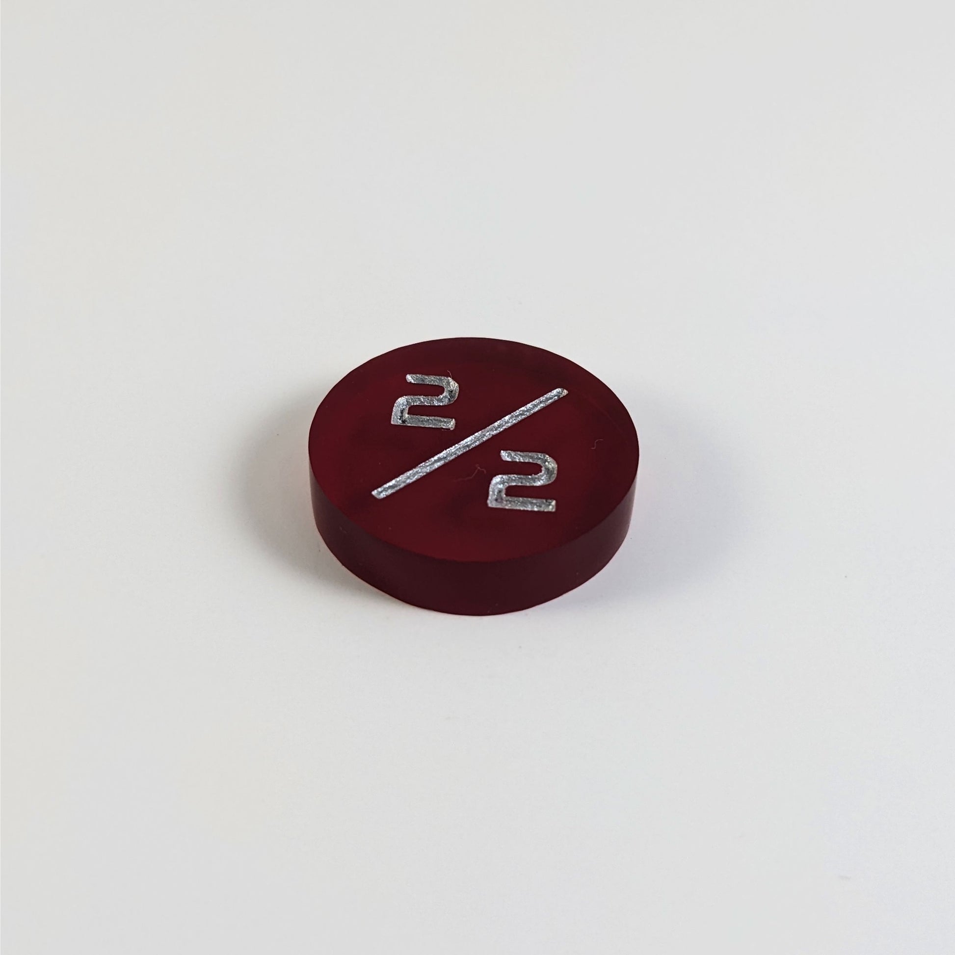 A low angle photo of a red 2/2 token with silver numbers sits on a white background.