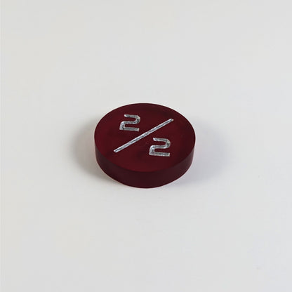 A low angle photo of a red 2/2 token with silver numbers sits on a white background.