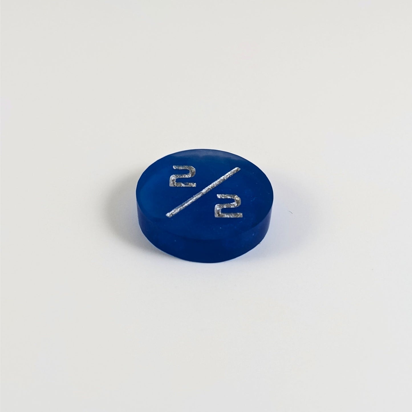 A low angle photo of a sapphire blue 2/2 token with silver numbers sits on a white background.