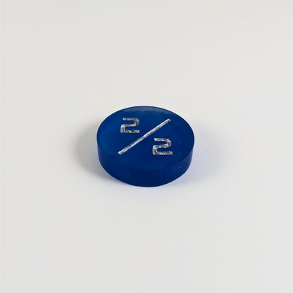 A low angle photo of a sapphire blue 2/2 token with silver numbers sits on a white background.