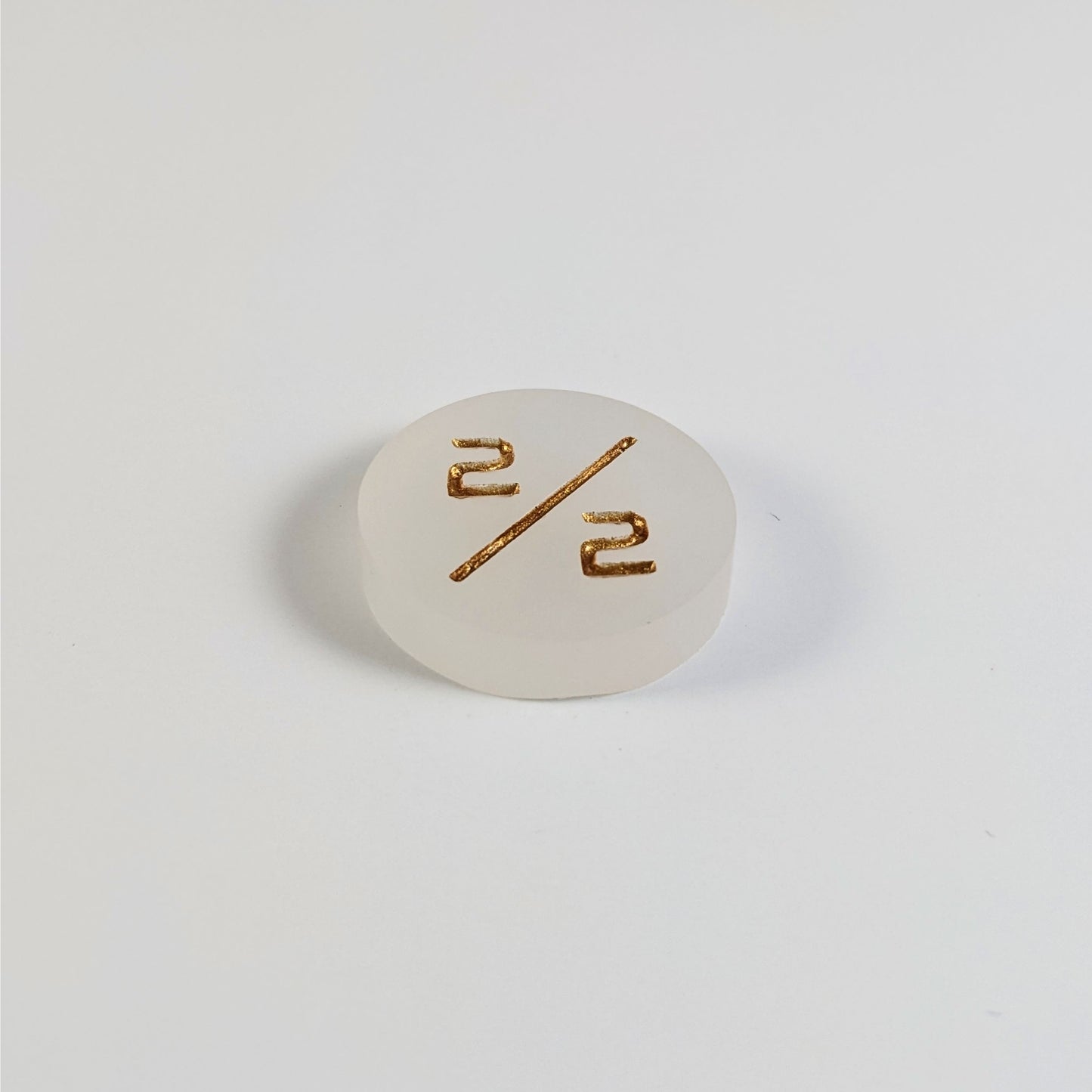 A low angle photo of a white 2/2 token with gold numbers sits on a white background.