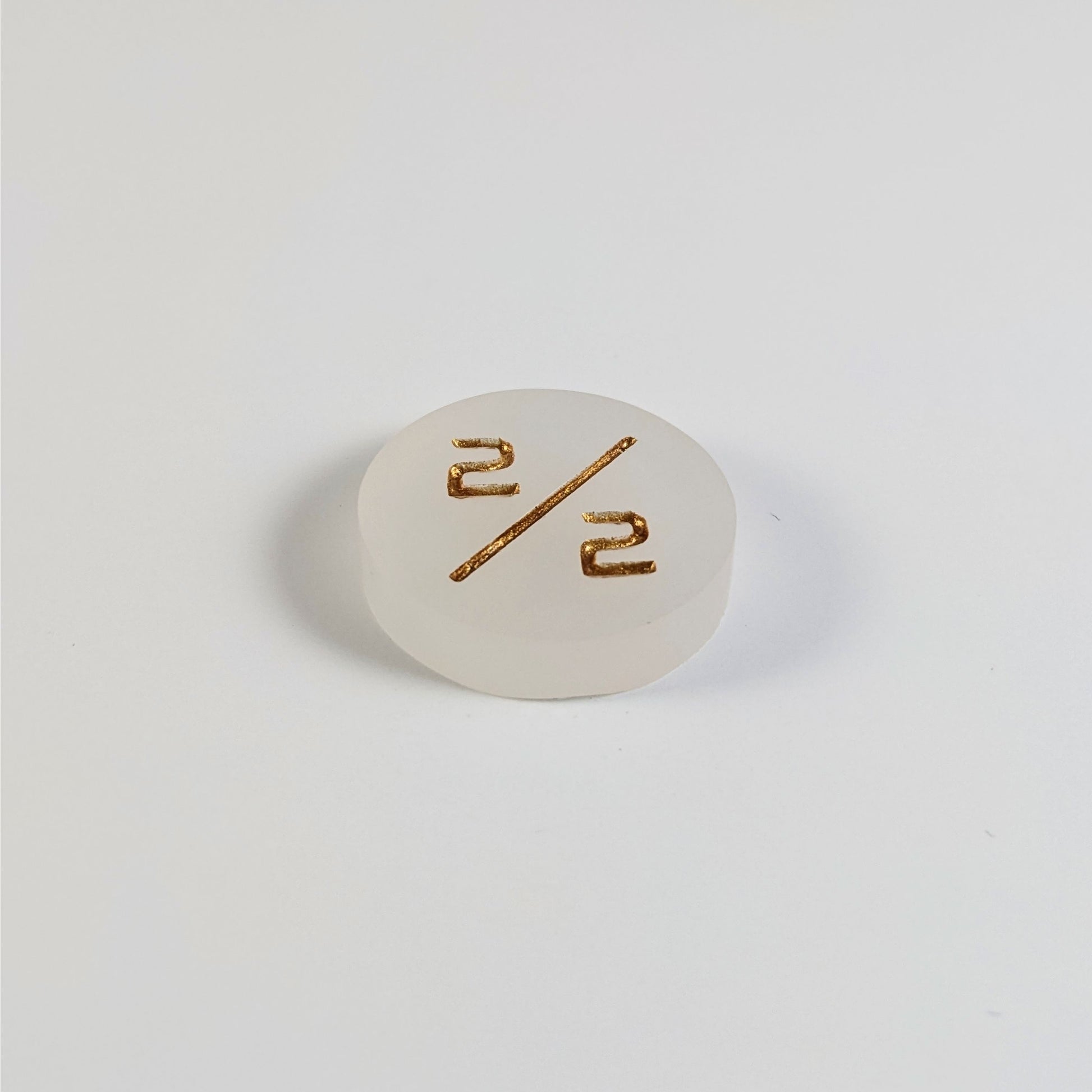 A low angle photo of a white 2/2 token with gold numbers sits on a white background.