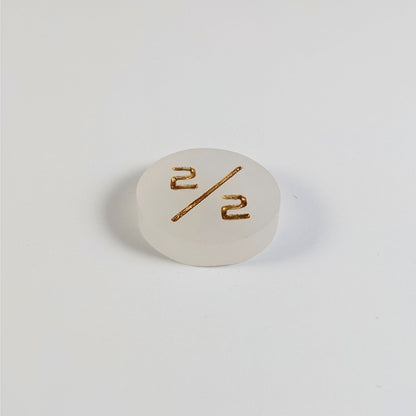 A low angle photo of a white 2/2 token with gold numbers sits on a white background.